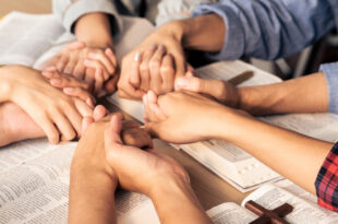 group praying over Bible - coming to Jesus