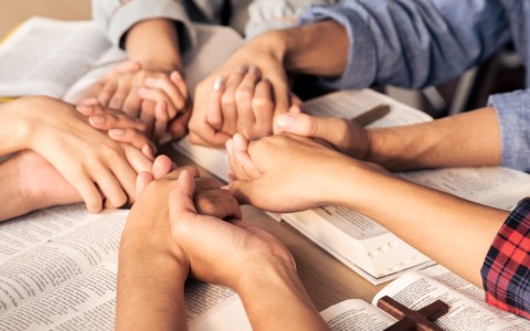 group praying over Bible - coming to Jesus